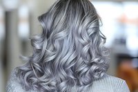 Trendy silver gray wavy hair with dimensional highlights shown from behind. Professional salon result demonstrates modern hair coloring and styling technique.