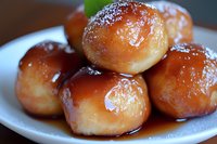Fresh homemade glazed donut holes stacked on white plate, dusted with powdered sugar and drizzled with sweet honey glaze, macro food photography.