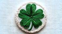 Green shamrock clover embroidered patch on white fabric background. Traditional Irish symbol handcrafted with detailed stitching for clothing decoration.