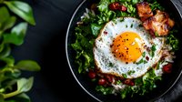 Healthy breakfast bowl with fried egg, fresh greens, cherry tomatoes and herbs in cast iron skillet. Nutritious morning meal for cooking blogs and menus.
