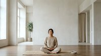 Woman in her 30s, East Asian ethnicity, wearing beige linen clothing, sitting in lotus position on wooden floor in minimalist meditation space with white walls, natural light, and potted plant for yoga and wellness.