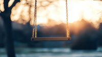 Empty wooden swing in park at sunset with golden sunlight and bokeh background creates nostalgic, peaceful atmosphere for concepts of childhood, loneliness or memories.