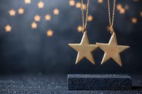 Golden star ornaments hanging on chains against dark background with blurred star-shaped bokeh lights, festive holiday decoration on glittery surface.