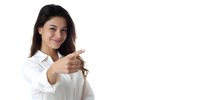 Young woman with long dark hair in white shirt pointing finger at viewer with friendly smile against white background.