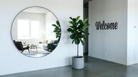 Modern minimalist entryway with round mirror, fiddle leaf fig plant, and welcome wall decor reflecting a bright Scandinavian-style living room.
