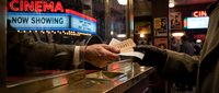 Hands exchanging movie tickets at cinema box office counter with neon signs and theater marquee in background. Entertainment venue.