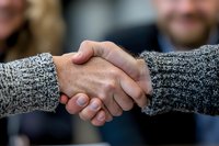 Close-up of firm handshake between two people wearing gray knit sweaters, symbolizing trust, agreement and business partnership in professional setting.