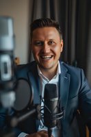 Cheerful Caucasian male podcaster in blue suit recording content with professional microphone setup, expressing genuine enthusiasm while speaking in home studio.