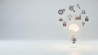 Glowing light bulb with business icons floating above on clean white background representing innovation, creativity and strategic thinking concepts.