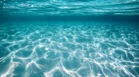 Underwater view of sunlight creating rippling patterns on sandy ocean floor through crystal clear turquoise water. Tranquil marine scene for nature backgrounds.