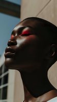 Young African woman with red eyeshadow makeup in artistic profile portrait showing elegant neck and facial features against soft natural lighting.