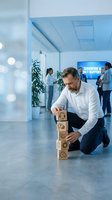 Businessman building wooden blocks with business icons in modern office environment representing strategy planning and corporate development.