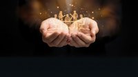 Cupped hands holding glowing wooden family figures with magical golden light and sparkles on dark background for protection and care concepts.