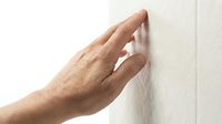Male hand touching smooth white wall surface showing tactile sensation and texture exploration in minimalist interior space.