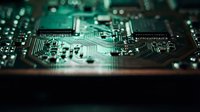 Close-up macro view of green computer circuit board with microchips, resistors and electronic components. Technology hardware background for tech projects.