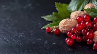 Fresh red currants with walnuts and green leaves on dark slate background for healthy eating and organic food concepts.