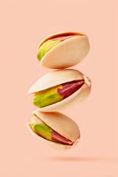 Flying pistachio nuts in shells, partially opened showing green and purple kernels inside against peachy pink background. Creative food levitation photography.