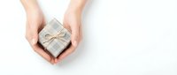 Female hands holding small wrapped gift box with ribbon on white background for holidays and special occasions.