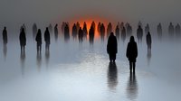 Silhouettes of people standing in misty water at sunset, creating mysterious atmospheric scene with reflections. Dark figures against orange glowing horizon in foggy landscape.