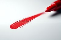 Red paint brush stroke on white surface creates dynamic diagonal composition with selective focus and shallow depth of field for artistic expression.