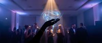 Hand holding glowing holographic brain with neural networks at technology conference with purple lighting and audience silhouettes in modern venue.