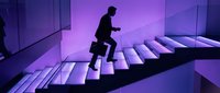 Silhouette of male professional climbing illuminated stairs in modern office environment with purple neon lighting, representing career growth and business success.