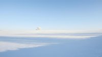 Aerial view of snow-covered landscape with distant mountain peak under clear blue sky, suitable for winter travel and nature backgrounds.