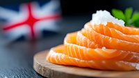 Fresh salmon sashimi slices arranged on wooden board with sea salt crystals and green garnish, British flag in soft focus background for food design.