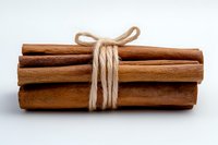 Bundle of aromatic cinnamon sticks tied with natural twine rope on white background, macro food photography for cooking and baking ingredients.