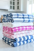 Stack of colorful plaid and striped kitchen towels neatly folded on marble countertop, featuring blue, pink, and white patterns for home decor.