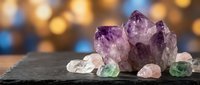 Amethyst crystal cluster with rose quartz and fluorite gemstones on dark slate, glowing bokeh background for spiritual healing concepts.