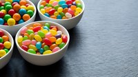 Colorful round candy balls in white ceramic bowls on dark wooden surface. Sweet confectionery treats for parties, celebrations and dessert displays.