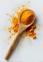 Vibrant turmeric powder in wooden spoon with raw turmeric roots and scattered spice on white background, popular in cooking and natural medicine.