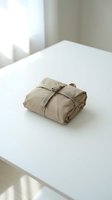 Folded beige linen fabric bundle tied with twine on white table in bright minimalist interior space with natural window light.