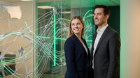 Professional business team of Caucasian woman and man standing confidently in modern office with digital network overlay graphics for corporate presentations.