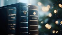 Stack of vintage leather-bound books against blurred Christmas tree lights creating magical bokeh effect in dark moody atmosphere. Cozy winter reading concept.