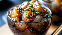Asian glazed meatballs with sesame seeds and green onions in glass bowl, savory appetizer dish with glossy sauce for restaurant menu and cooking content.