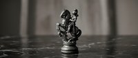 Black and white chess knight piece with small figure climbing on top, symbolizing ambition, strategy, and business growth on dark surface.