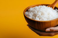 White cooked rice in wooden bowl held by hand against yellow background. Suitable for food, cooking, nutrition, and recipe content.