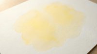 Yellow watercolor paint stain on white textured paper creating abstract artistic background for creative projects and design work.