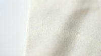 Soft cream colored fabric texture with gentle folds and natural wrinkles creating elegant shadows and highlights for textile and fashion design projects.