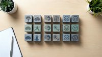Wooden rubber stamps with nature and emoji symbols arranged on desk with plants and notebook for crafting and office projects.
