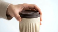 Caucasian hand holding an eco-friendly reusable coffee cup with brown lid on white background, sustainable zero waste lifestyle concept.
