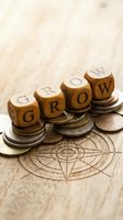 Wooden letter blocks spelling GROW stacked on coins with compass design on wood surface representing financial growth and investment strategy development.