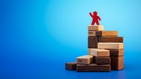 Red figure climbing stacked wooden blocks against blue background, representing career growth, success, achievement, and business advancement through education and development.