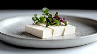 Fresh tofu slices garnished with microgreens on ceramic plate for healthy plant-based cuisine and vegetarian cooking concepts.