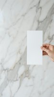 Hand holding blank white card against marble textured background, mockup for business cards, invitations, or promotional materials.