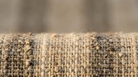Natural burlap fabric texture with rough woven fibers and frayed edges on neutral background for rustic craft and packaging design projects.