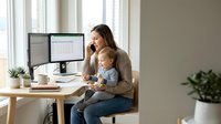 Young mother working from home office while holding baby, multitasking professional woman balancing career and childcare in modern workspace.