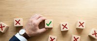 Hand selecting wooden cube with green checkmark among red X marks on desk representing choice, decision making and quality selection in business.